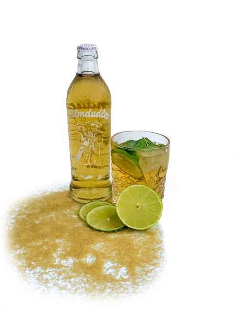 Almdudler-Flasche neben einem Longdrink mit Minze, Limette und Eis, garniert mit Limettenscheiben