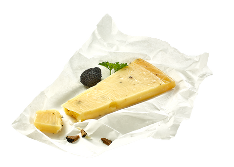 Trüffelkäse-Ecke auf Pergamentpapier mit Trüffelknolle, Petersilie und Trüffelspänen